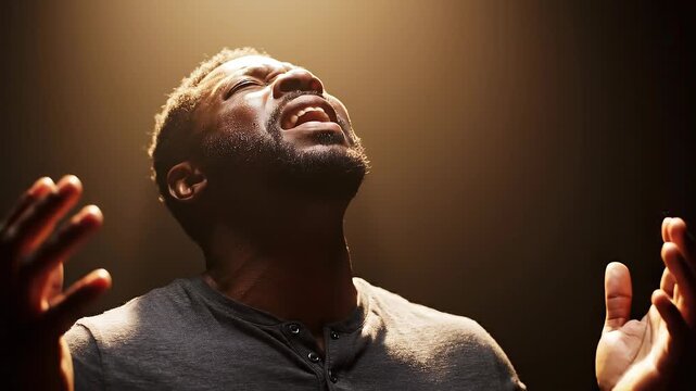 Emotional man with closed eyes raising hands in worship or prayer with warm light background