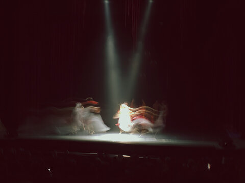 Artistic motion blur of dancers performing on a dark theater stage under spotlights. Concepts of movement, energy, and ghosting effect.