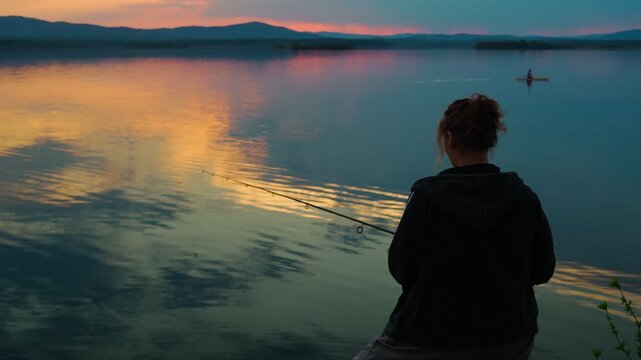 A female fisherman is fishing on a lake against the backdrop of an unusually beautiful sunset. Fishing and outdoor recreation. A healthy lifestyle. Real footage without staged elements.