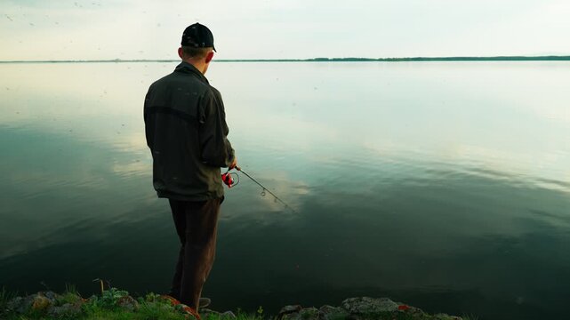 A man is fishing on a lake, surrounded by a swarm of blood-sucking mosquitoes that are causing him discomfort. Real footage without staged elements.