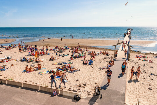 Crowded sand beach with a pier and People sunbathing and relaxing by the sea