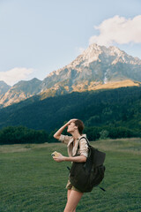 Obraz premium Woman hiking outdoors with backpack, enjoying nature and mountain scenery, sunlit field, casual apparel, sense of adventure, travel, relaxed lifestyle, fresh air.