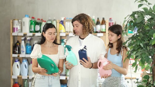 Friendly modern family of three using smartphones to scan barcode on cleaning supplies bottles in local supermarket, looking for discounts, checking for digital coupons and special offers