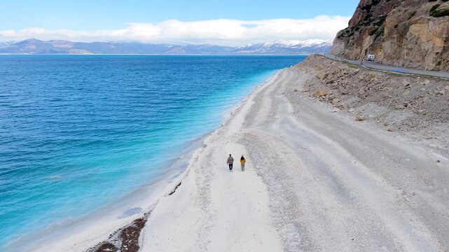 Experience the breathtaking shores of Salda Golu Lake in Turkey as two travelers stroll along the pristine white sand beach and clear turquoise waters. a couple walking on the beach