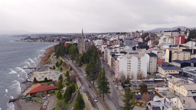 Cloudy skies hover over the coastal cityscape of San Carlos de Bariloche, showcasing urban development alongside the shoreline. Suitable for weather or urban planning projects.