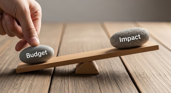 Hand balancing budget and impact stones on wooden seesaw scale in natural lighting