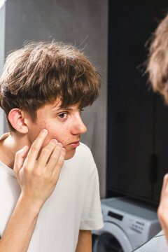 Teenage boy looking in the mirror and checking acne on his face