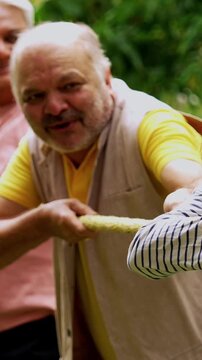 Senior playing tug of war in garden, Indian Asian elderly friends enjoying outdoor physical activity with rope, laughing and pulling together as part of fun reunion game amid green nature