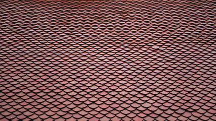 Traditional red terracotta roof tiles of a Thai Buddhist temple showing a scale-like pattern and texture. © Ranta Images