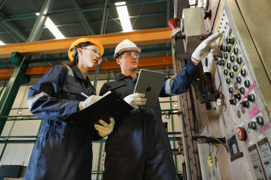 Engineer man and woman worker working with tablet computer and checking machine in warehouse for production supply