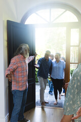 Obraz premium Couple walking into foyer, senior host holding dark wood door, sunlight flooding entry