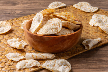 Fototapeta premium Crispy tempeh chips arranged in a wooden bowl on a traditional woven mat and rustic table