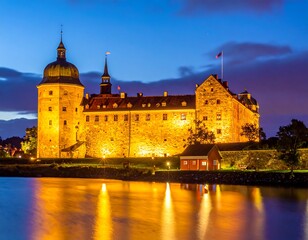 Fototapeta premium A large illuminated castle by a body of water at dusk