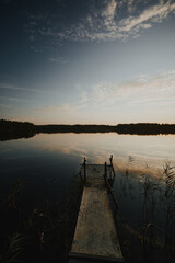 Fototapeta premium Fishing pier on a forest lake lit but the setting sun