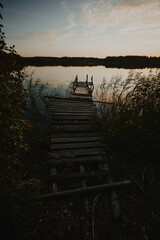 Fototapeta premium Fishing pier on a forest lake lit but the setting sun