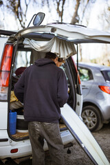 Naklejka premium Man standing by open van, preparing surfboard for travel adventure