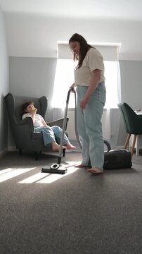 Mother vacuum cleaning while talking with daughter eating apple