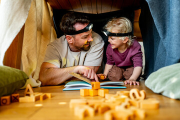 Fototapeta premium Dad and child building and reading book in cozy blanket fort.