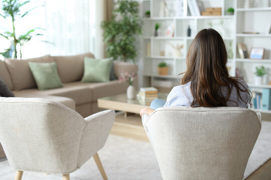 Back view of a woman sitting alone on armchair at home