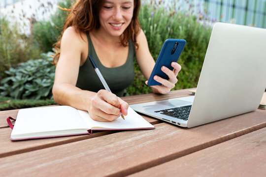 Woman working remotely outdoors using laptop and smartphone