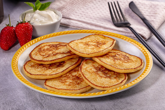 Homemade golden pancakes on plate with fresh strawberries and sour cream