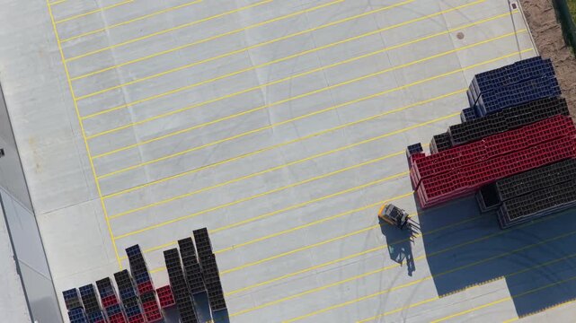 Top down view of forklift moving pallets in material warehouse yard, industrial logistics and supply chain distribution, aerial backward flight, 4K Cinematic