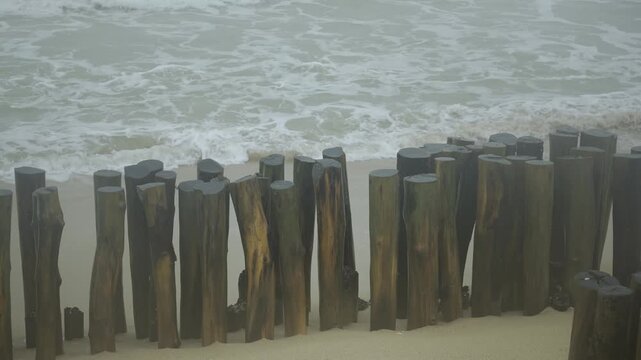 waves crashing against wooden sea wave breaker on a coastal sand beach, creating dramatic white splashes and patterns from open sea ocean, scary beach sea in rainny weather of southern thailand