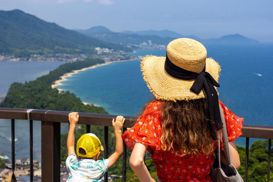 Amanohashidate, Kyoto Prefecture, Japan, Summer, Lady tourist in hat with her small son. Facing the sea and sand spit. View from the hill.