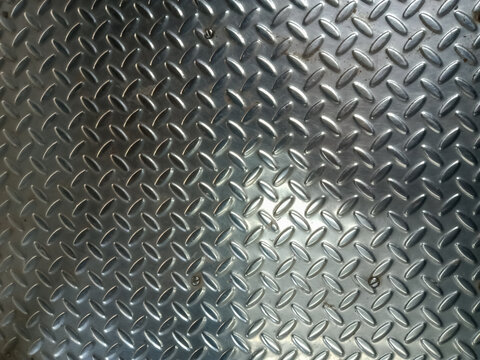 Abstract background a diamond plate, a type of metal sheet characterized by a regular pattern of raised diamonds or lines on one side. The surface is metallic and reflective