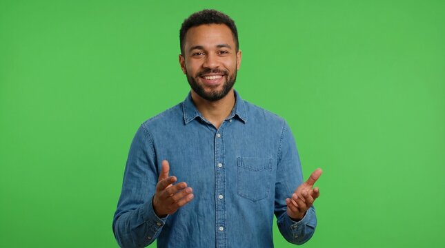 Interactive man in a denim shirt gesturing with hands and explaining while smiling on a green screen background for online course promos distance learning and virtual technical support tutorials.