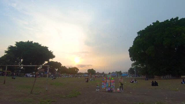 Sunset landscape of Alun-Alun Selatan Yogyakarta with people, families, and soap bubbles in the open field. Large trees and community recreation at the iconic city landmark