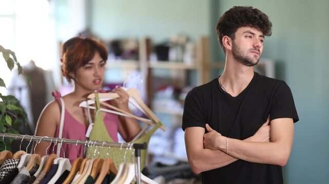 Guy tired of shared shopping with girlfriend in fashion store