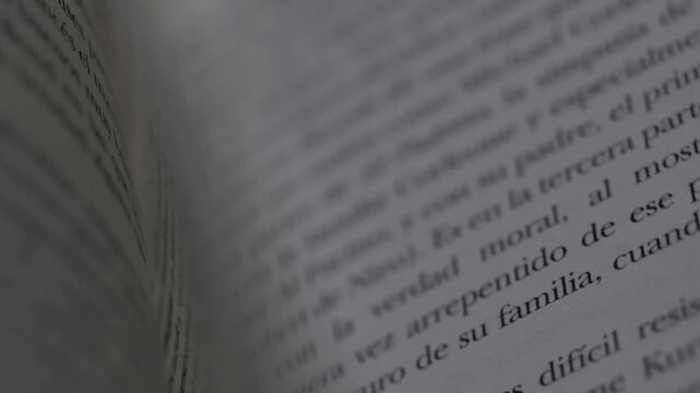 Pages of book quickly turning, revealing text, close up shot of a person turning pages of a book, revealing text on each page with blurred background.