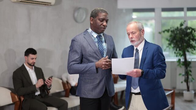 Queue of applicants is waiting in reception room, senior male HR manager is talking to African man office-seeker. Job interview, labor policy, elimination of unemployment. 