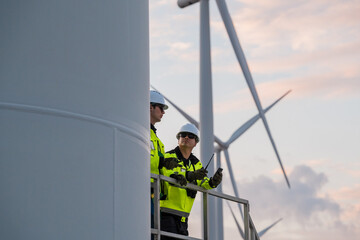 Diverse industrial technicians with tablet and walkie-talkie inspecting wind farm during evening shift, green energy concept. © VStudio