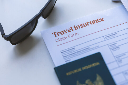 High angle view of travel insurance claim form with passport, toy airplane, sunglasses, and straw hat on white surface
