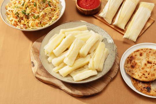 Boiled yuca on plate of Latin American table with arepas, pupusas, humitas, curtido
