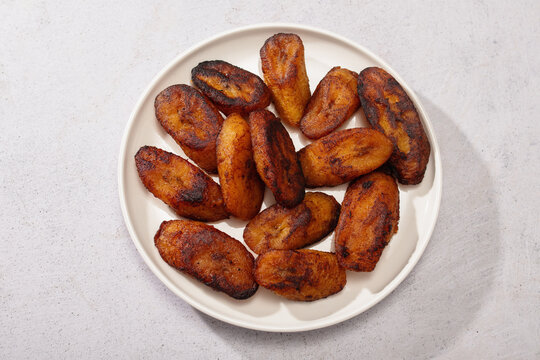 Fried sweet plantain tajadas on white plate, light background.