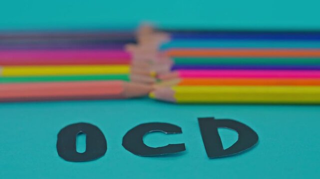 Close-Up Slow Motion Rack Focus From Sharp Colored Pencil Tips To "Ocd" Text On Turquoise Background