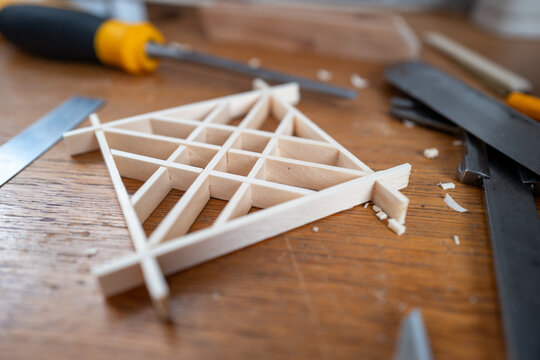 Small wooden Kumiko Chochin izutsu tsugi coaster aid on a workbench surrounded by chisel, a saw and caliper, illustrating hands‑on woodworking, model making, carpentry skills and DIY craft project.