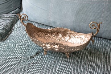 Copper antique gondola bowl. The antique metal gondola bowl is on top of the sofa. Inheritance or family heirloom. Souvenirs. No people, nobody. Horizontal photo. © Burak