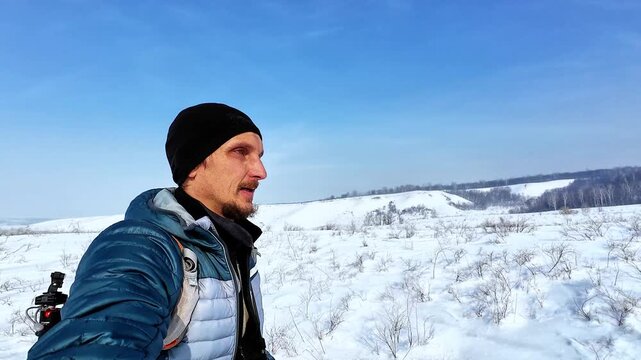 Caucasian Man Vlogging From Snowy Ridge With Ski Poles And Backpack, Facing Camera And Describing Route, Clear Blue Sky And Vast Snowfield, Energetic Narration And Scenic Panorama