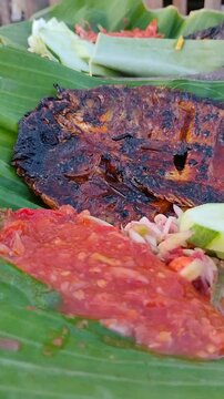 Cinematic close-up of Indonesian Grilled Gourami Fish (Ikan Gurame Bakar) with spicy sambal on a banana leaf