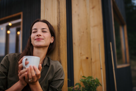 Young woman with coffee outdoors, weekend away in container house in countryside.