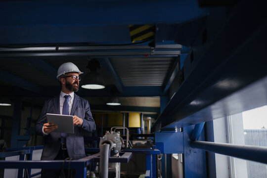 Engineer in hard hat supervising factory operations with digital tablet.