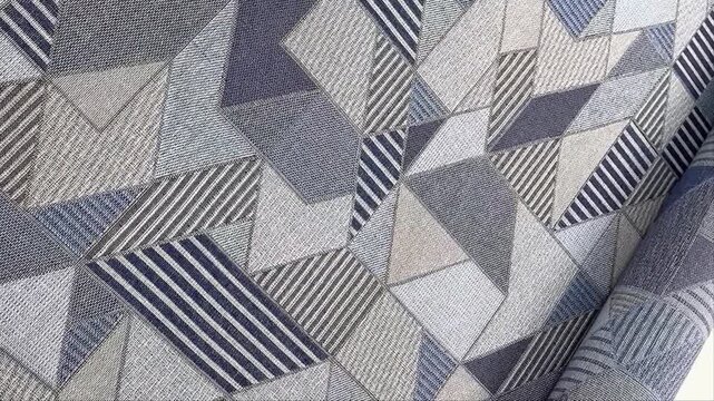 A heavy duty upholstery fabric features a dynamic grey and blue geometric pattern with abstract triangles and stripes providing a modern textile solution for furniture and home decor