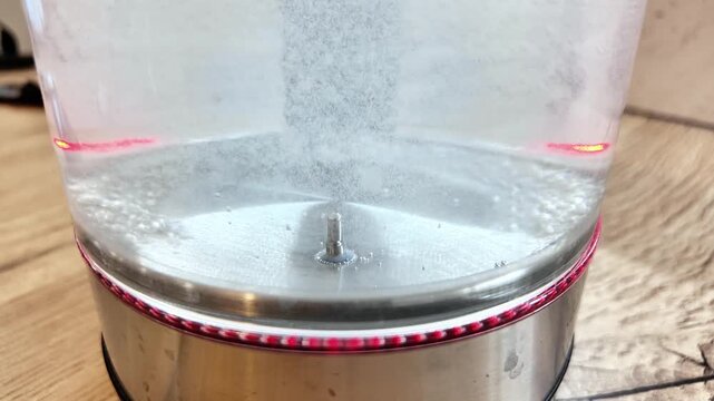 Glass Kettle Central Vortex Forming With Rising Microbubbles, Kitchen Countertop View Capturing Swirl Motion, Stainless Base And Red Led Accent Create Dynamic Experimental Feel