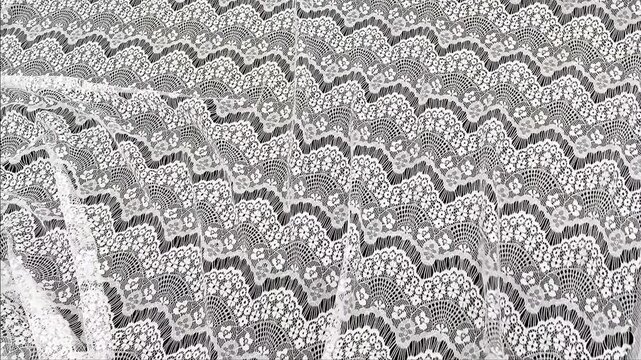 A delicate white lace material features ornate floral embroidery and scalloped edges creating a classic aesthetic for bridal gowns wedding decor and high end fashion apparel design