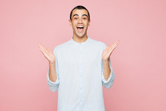 Young shocked surprised excited amazed happy middle eastern man he wear casual blue cotton shirt look camera spread hands isolated on plain pastel light pink wall background studio. Lifestyle concept.