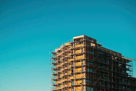 Urban apartment building under construction with exterior scaffolding against blue sky